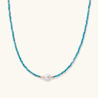 Dainty teal apatite beaded necklace with a single freshwater pearl centerpiece flanked by two small gold beads, adjustable gold clasp.