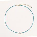 Dainty teal apatite beaded necklace with a single freshwater pearl centerpiece flanked by two small gold beads, adjustable gold clasp.