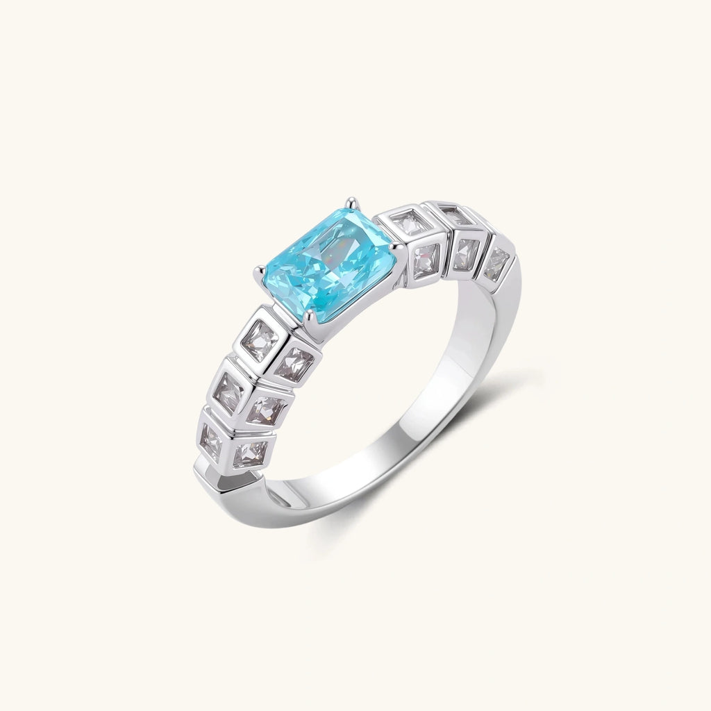 Geometric silver-plated ring with rectangular aqua cubic zirconia center and square crystal details on adjustable band.
